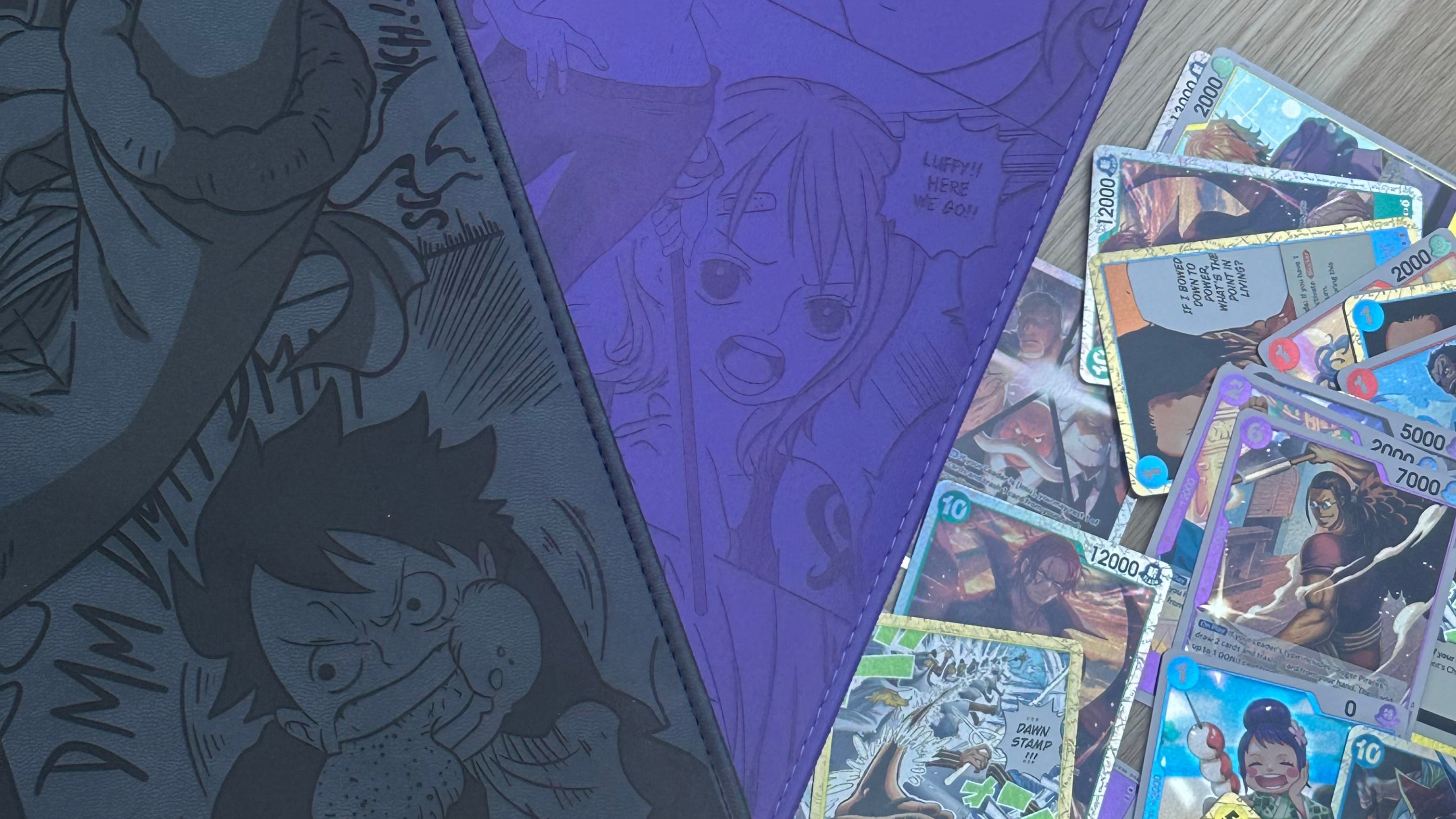 Two gaming mats with anime designs on a wooden surface with trading cards scattered around.